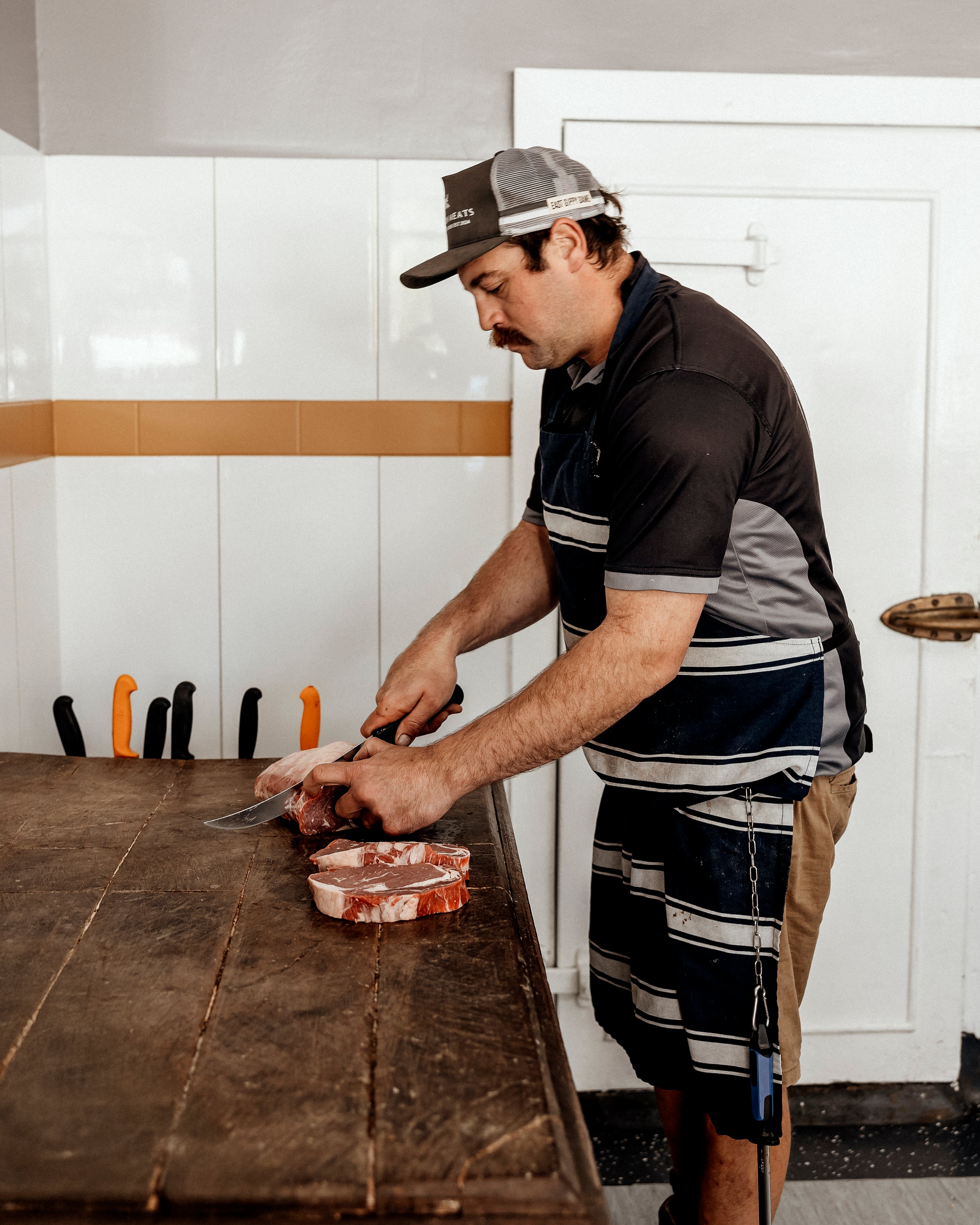 Man cutting meat on a wooden counter in a kitchen.