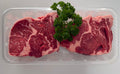 Two raw steaks on a clear plastic tray with fresh parsley on a white background