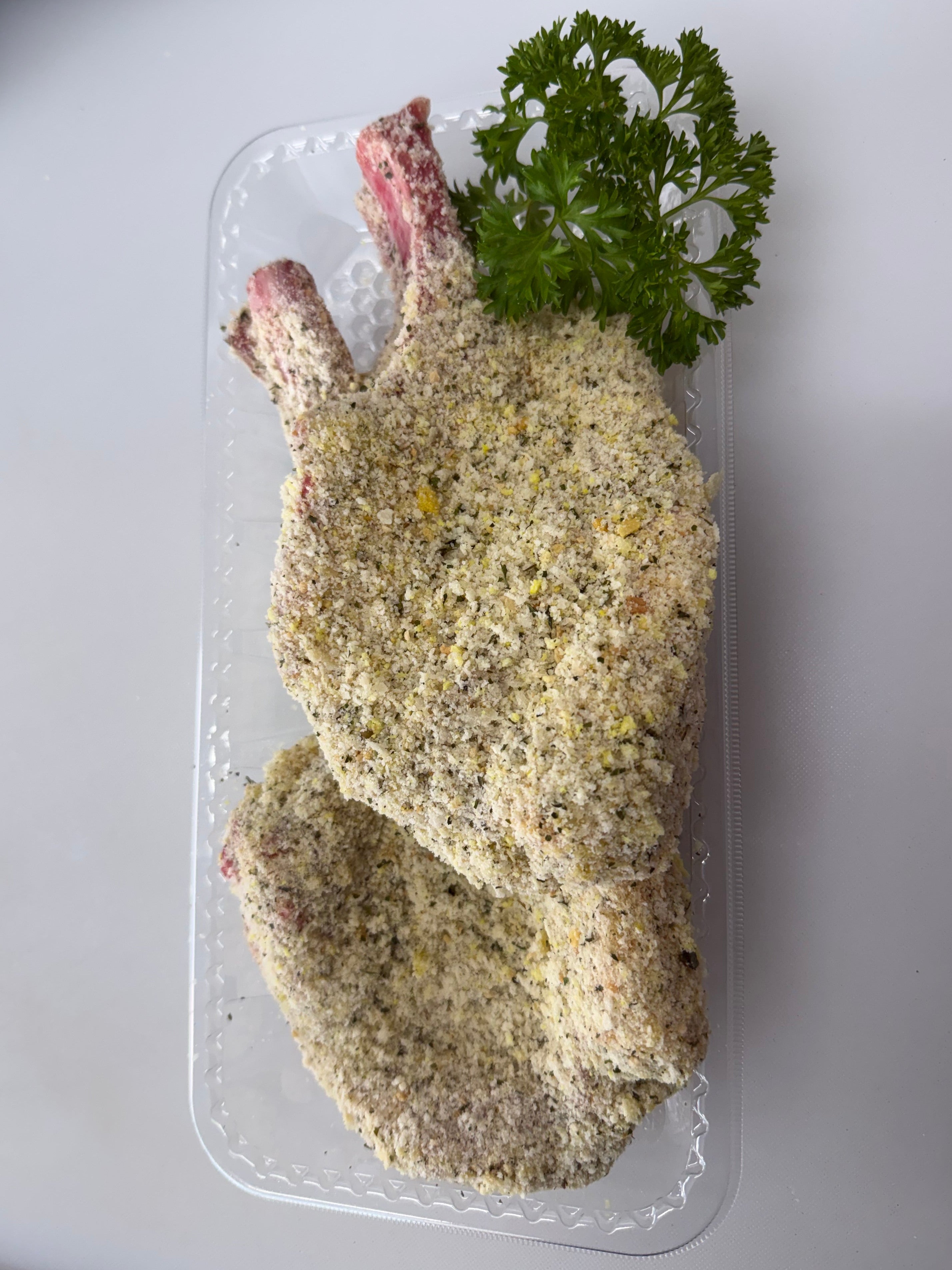 Raw chicken breast with breadcrumb coating on a clear plastic tray with parsley garnish.
