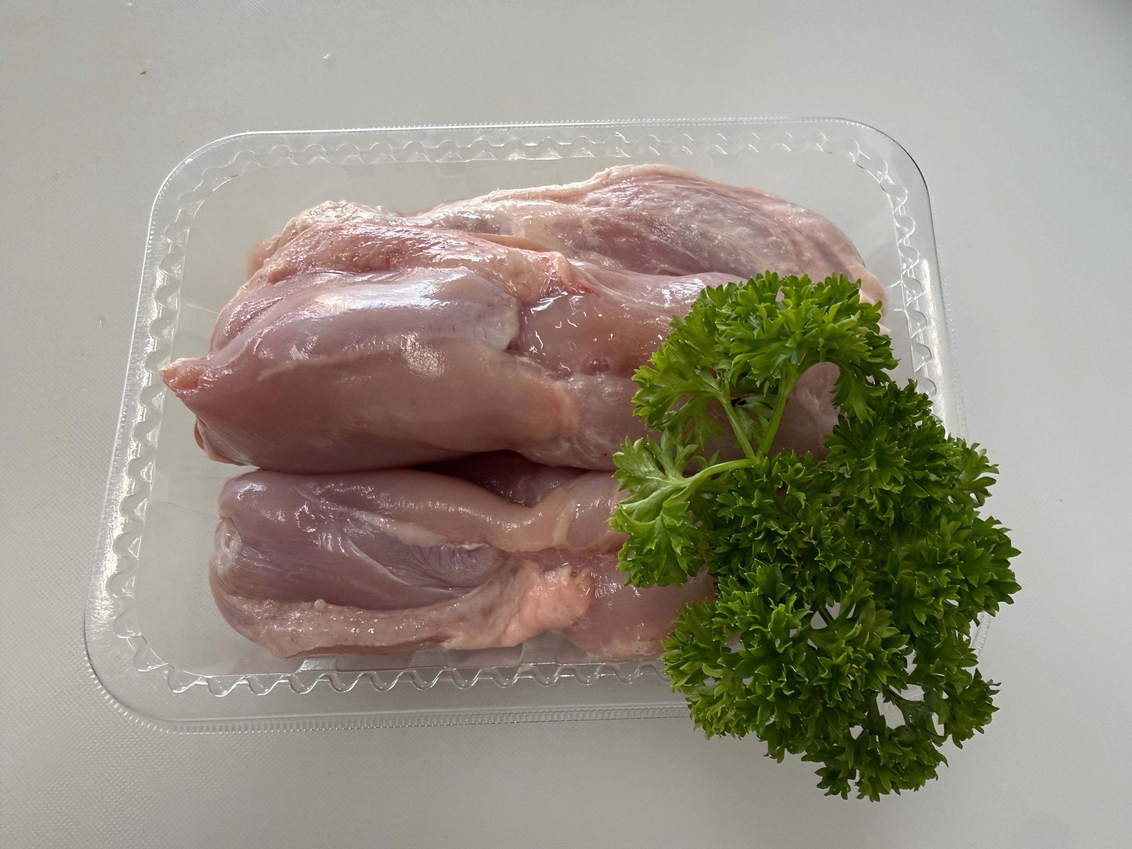 Raw chicken breasts with parsley on a clear plastic tray against a white background