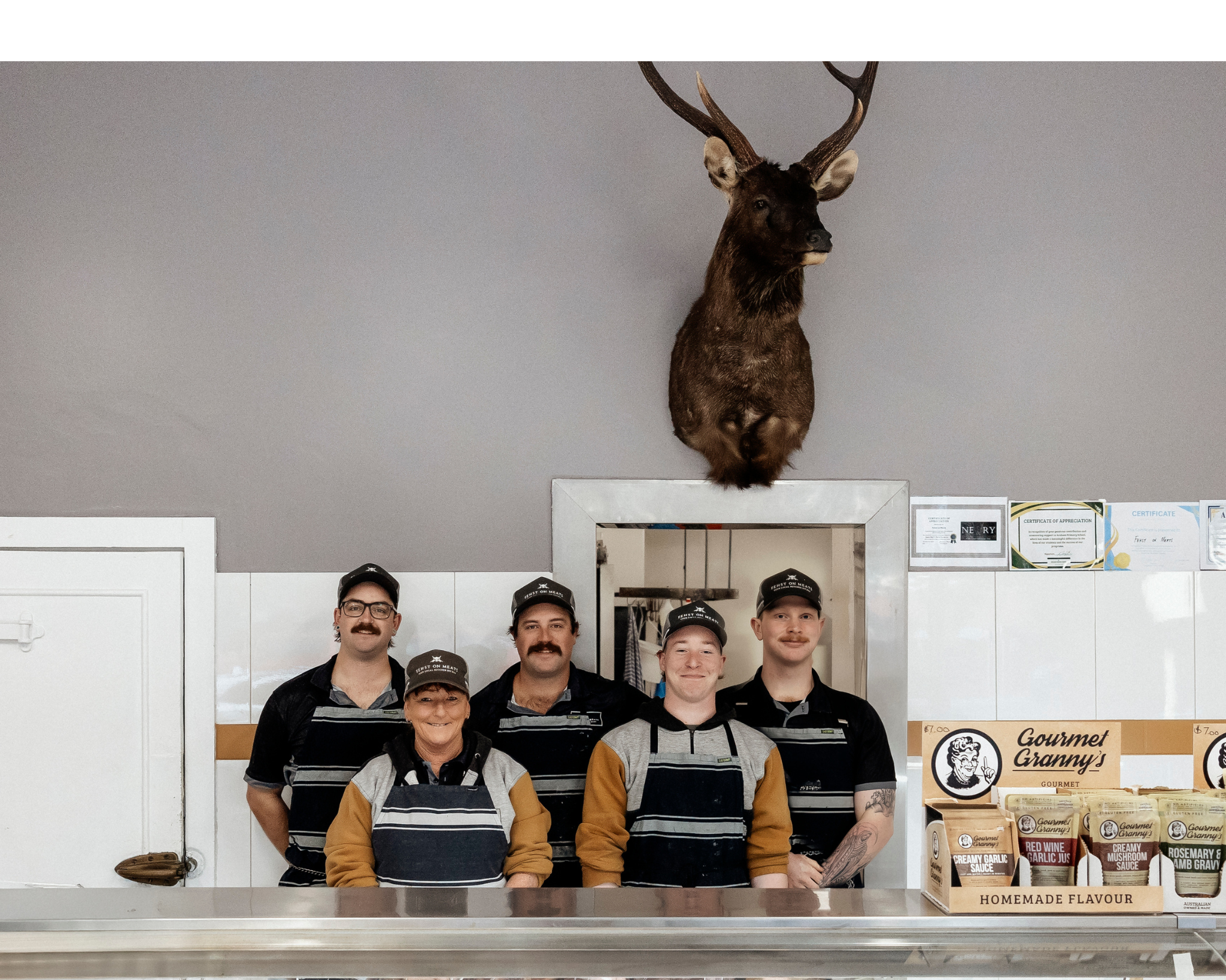 Five people in a kitchen with a deer head mounted on the wall.